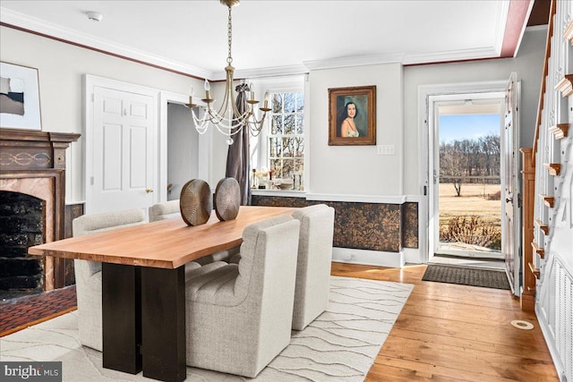 dining space featuring a chandelier, ornamental molding, light wood finished floors, and a premium fireplace