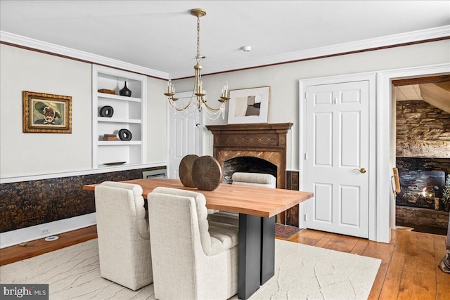 dining area featuring light wood-style floors, built in shelves, a chandelier, and crown molding