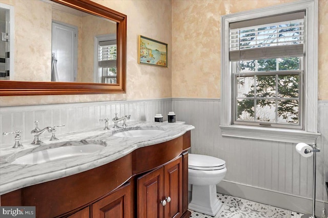 bathroom featuring wainscoting, a sink, toilet, and double vanity