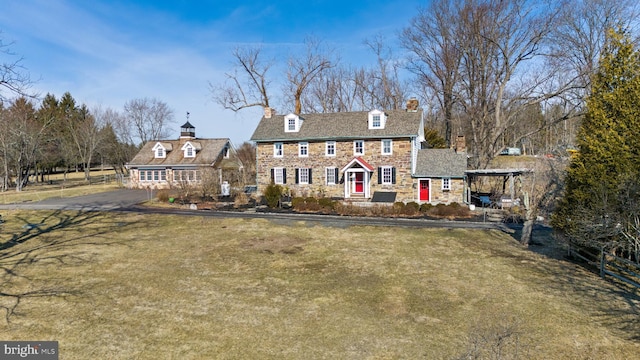 colonial home with stone siding, a chimney, and a front lawn