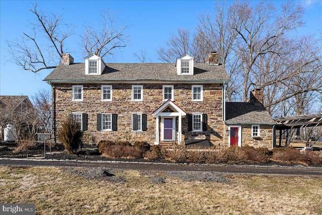 view of front facade featuring a shingled roof, stone siding, a chimney, and a pergola