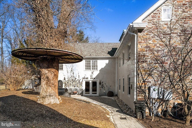 rear view of property with a shingled roof, french doors, and stucco siding