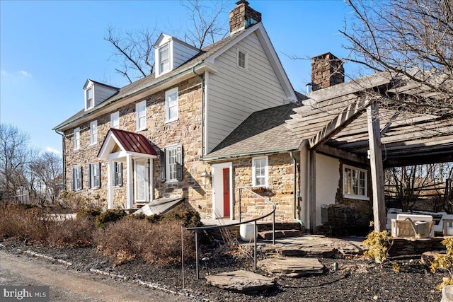 view of front of home with a shingled roof, stone siding, and a chimney