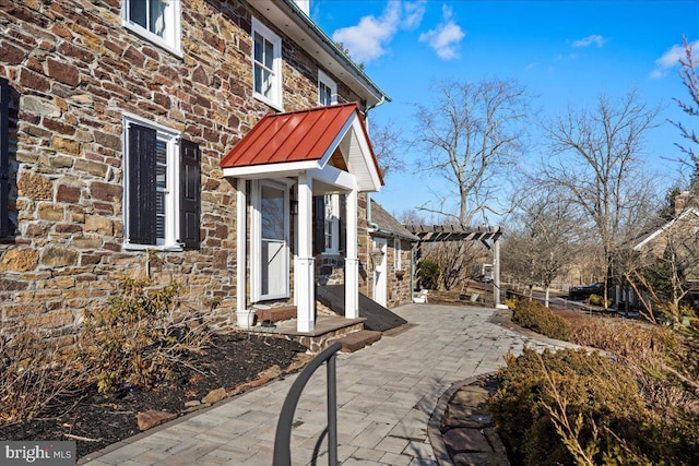 exterior space with a patio, stone siding, metal roof, a standing seam roof, and a pergola