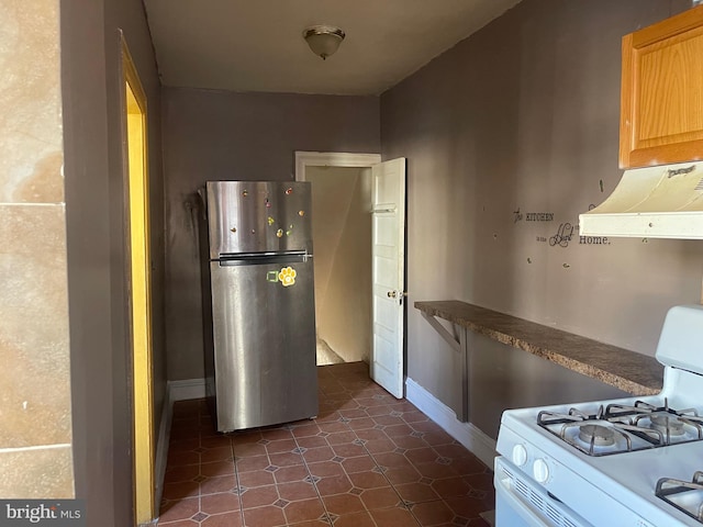 kitchen featuring extractor fan, white gas range oven, dark tile patterned floors, stainless steel refrigerator, and light brown cabinets