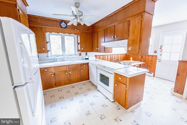 kitchen with white appliances, a baseboard heating unit, sink, wooden walls, and ceiling fan