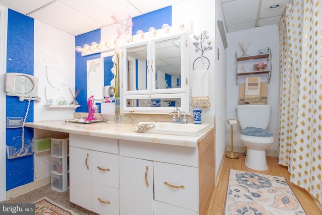 bathroom featuring wood-type flooring, vanity, toilet, and a drop ceiling