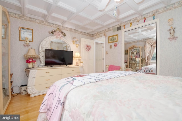 bedroom featuring beamed ceiling, a closet, light hardwood / wood-style flooring, and coffered ceiling