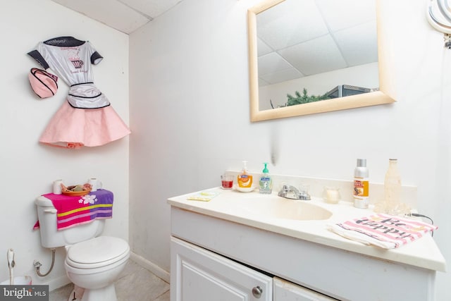 bathroom featuring toilet, vanity, a drop ceiling, and tile patterned floors