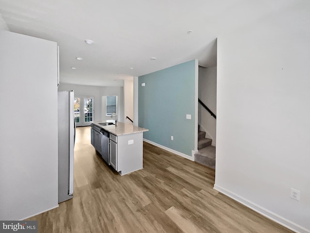 kitchen with appliances with stainless steel finishes, sink, light wood-type flooring, and a center island with sink