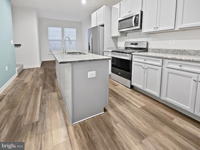 kitchen featuring appliances with stainless steel finishes, sink, white cabinets, light hardwood / wood-style flooring, and a center island with sink