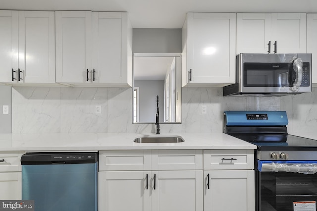 kitchen with backsplash, sink, light stone countertops, white cabinets, and appliances with stainless steel finishes