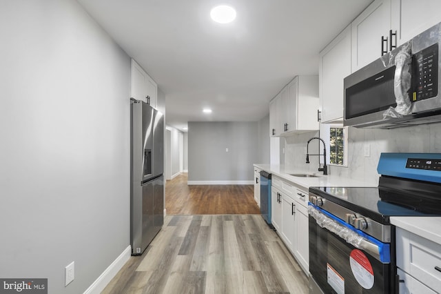 kitchen with appliances with stainless steel finishes, sink, backsplash, white cabinets, and light hardwood / wood-style flooring