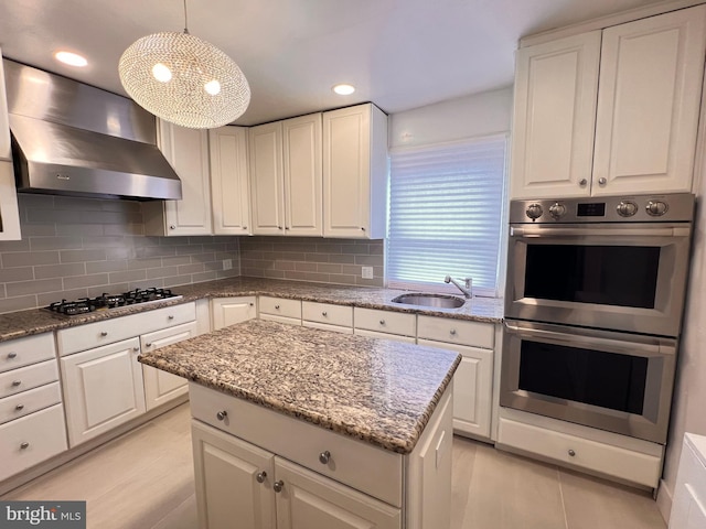 kitchen featuring sink, wall chimney exhaust hood, pendant lighting, white cabinets, and appliances with stainless steel finishes