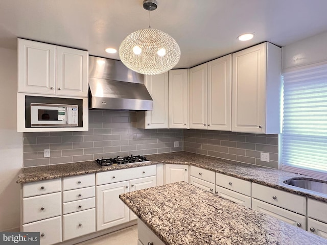 kitchen featuring wall chimney range hood, gas cooktop, pendant lighting, decorative backsplash, and white cabinets