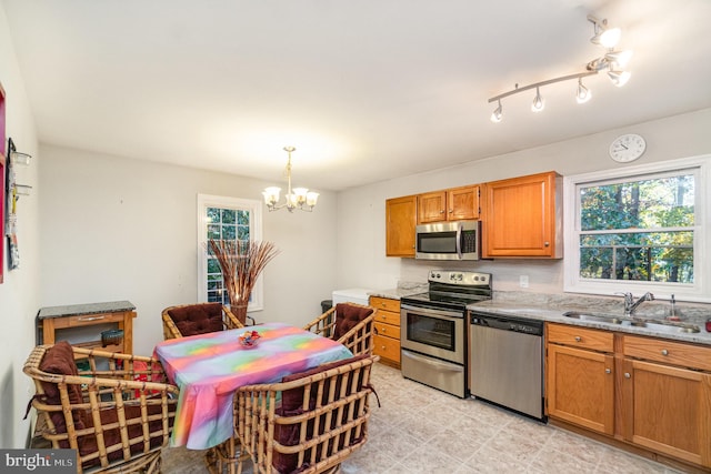 kitchen featuring stainless steel appliances, sink, a notable chandelier, pendant lighting, and light stone counters