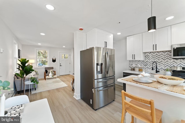 kitchen with appliances with stainless steel finishes, decorative light fixtures, light wood-type flooring, and white cabinets