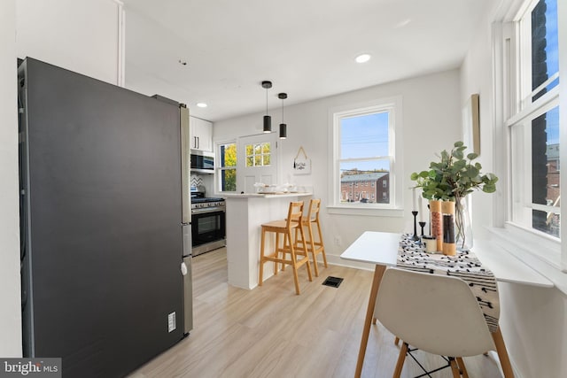 kitchen with light hardwood / wood-style flooring, a kitchen bar, decorative light fixtures, white cabinetry, and appliances with stainless steel finishes