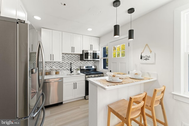 kitchen featuring kitchen peninsula, white cabinets, a kitchen bar, sink, and stainless steel appliances