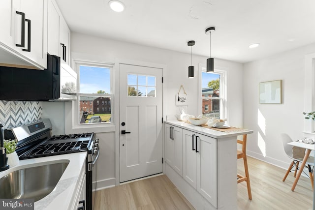 kitchen with kitchen peninsula, white cabinetry, stainless steel gas stove, and a wealth of natural light