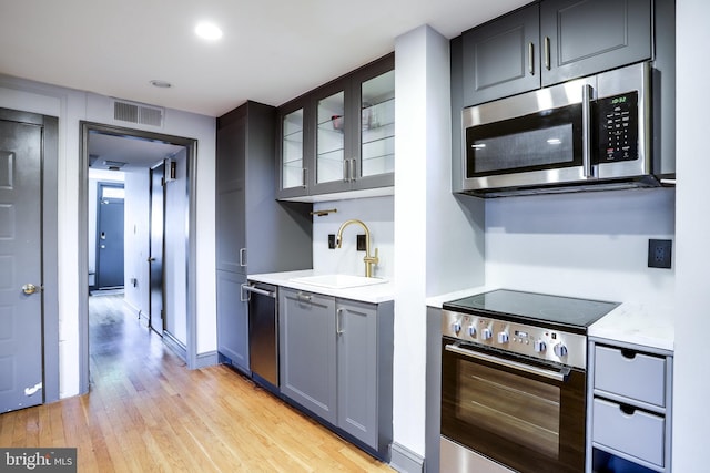 kitchen featuring light stone countertops, light hardwood / wood-style floors, appliances with stainless steel finishes, and sink