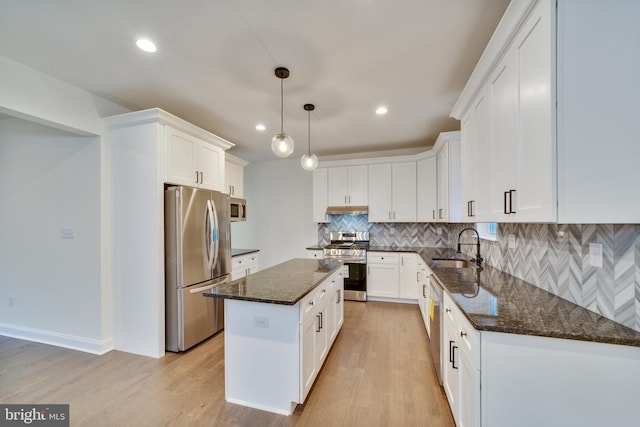 kitchen with appliances with stainless steel finishes, white cabinets, pendant lighting, and a kitchen island