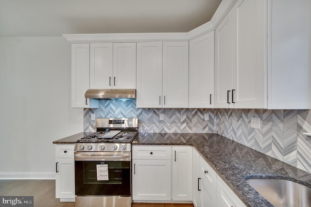 kitchen with white cabinetry, dark stone counters, backsplash, and gas range