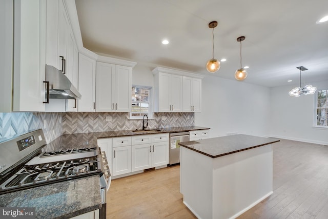 kitchen with white cabinets, hanging light fixtures, appliances with stainless steel finishes, a center island, and ventilation hood