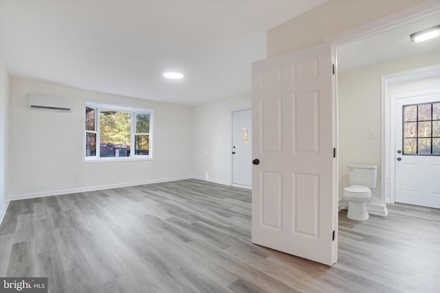 spare room featuring an AC wall unit, light hardwood / wood-style floors, and plenty of natural light