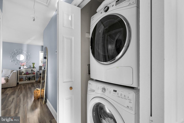 clothes washing area with dark wood-type flooring and stacked washer and clothes dryer