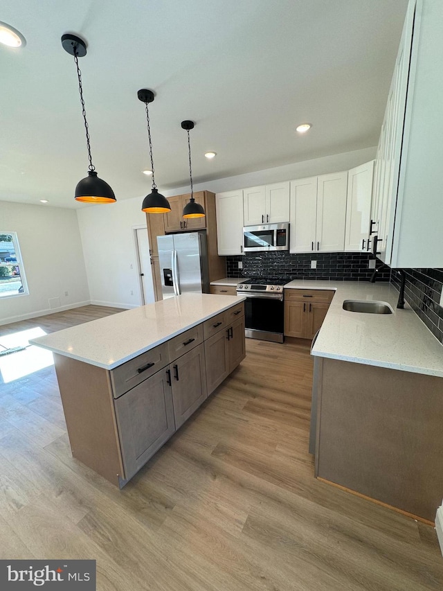 kitchen featuring a center island, white cabinets, pendant lighting, appliances with stainless steel finishes, and light stone counters