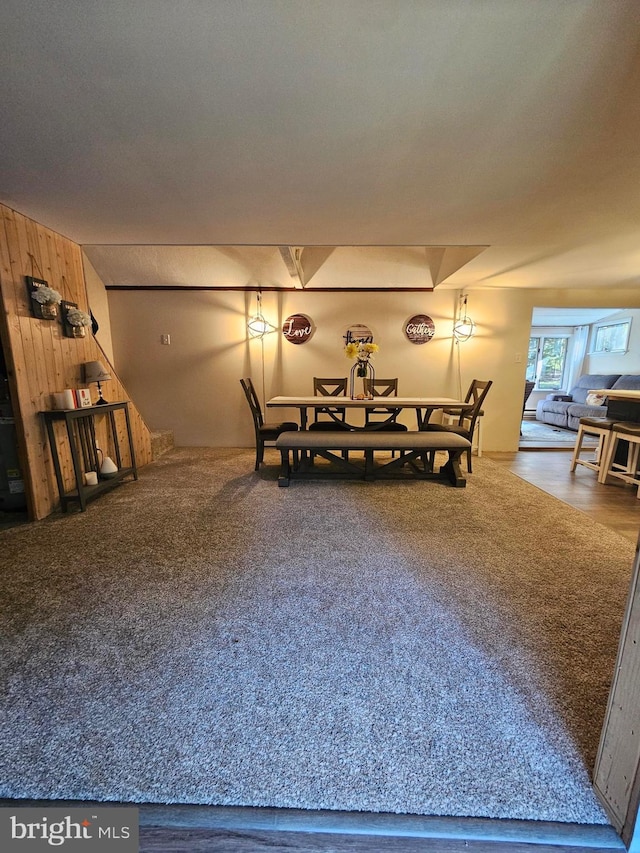 carpeted dining area featuring wooden walls