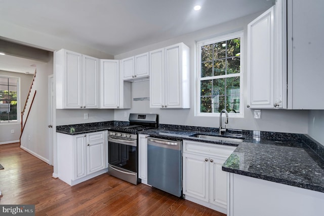 kitchen with appliances with stainless steel finishes, sink, dark stone counters, white cabinets, and dark hardwood / wood-style floors