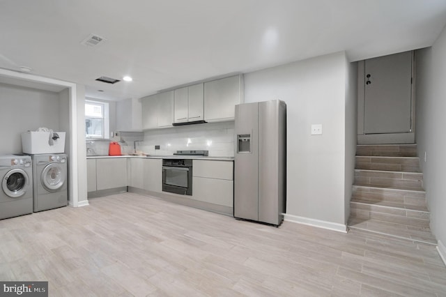 kitchen featuring appliances with stainless steel finishes, washer and dryer, and light wood-type flooring