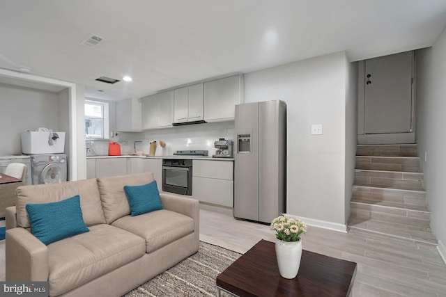 living room featuring stacked washer and dryer, sink, and light hardwood / wood-style flooring