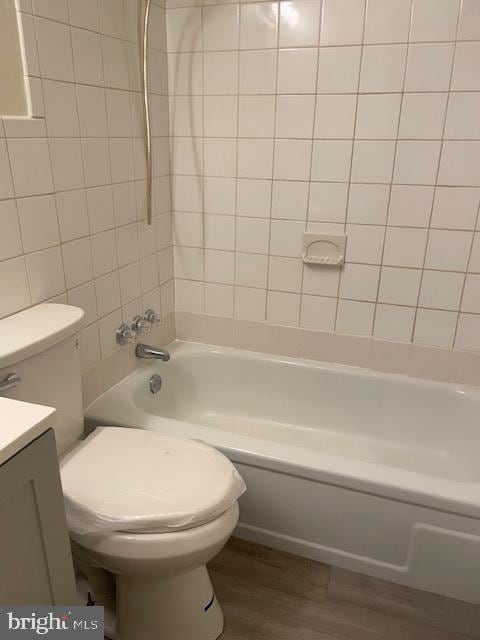 full bathroom featuring wood-type flooring, toilet, tile walls, tiled shower / bath, and vanity