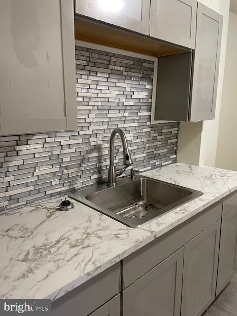 kitchen featuring decorative backsplash, light stone countertops, sink, and gray cabinetry