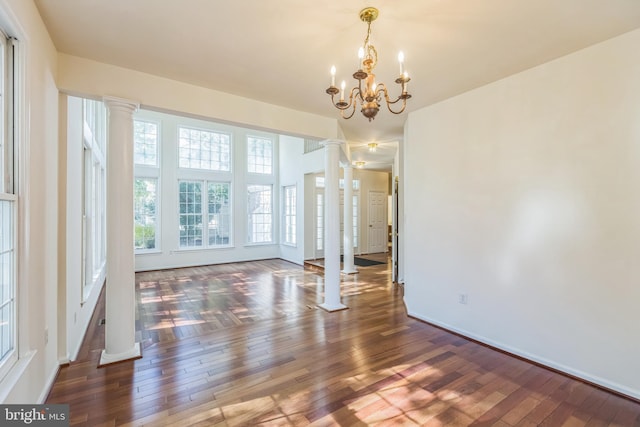 unfurnished dining area with decorative columns, dark hardwood / wood-style floors, and a chandelier