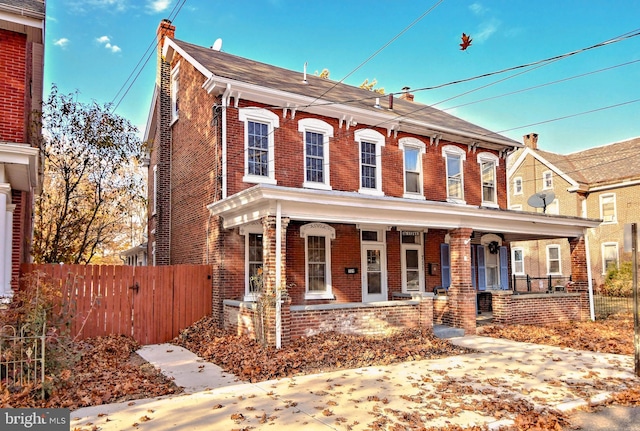 italianate-style house featuring brick siding, a chimney, covered porch, and fence