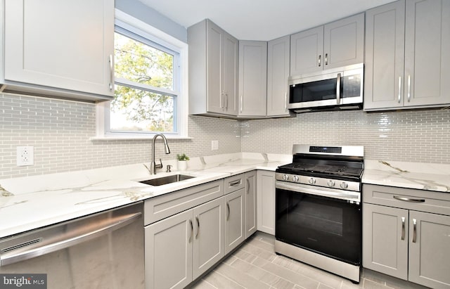 kitchen with stainless steel appliances, gray cabinetry, a sink, and decorative backsplash