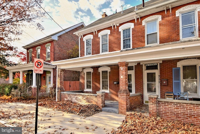 view of front facade featuring brick siding, covered porch, and a chimney