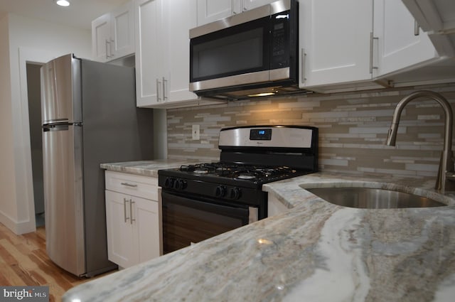 kitchen with light hardwood / wood-style flooring, stainless steel appliances, sink, white cabinets, and light stone counters