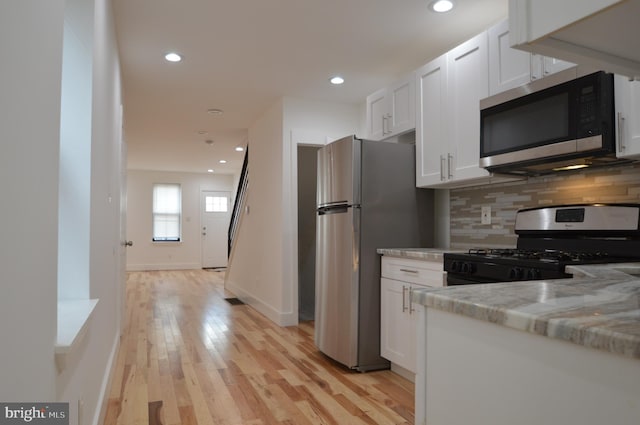 kitchen with backsplash, white cabinetry, light hardwood / wood-style floors, stainless steel appliances, and light stone counters