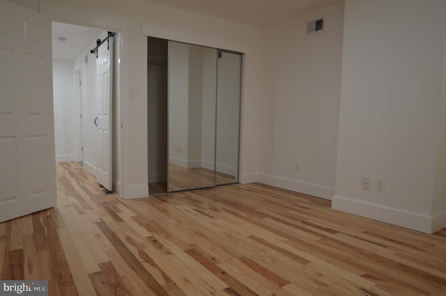 unfurnished bedroom with a closet, a barn door, and light wood-type flooring