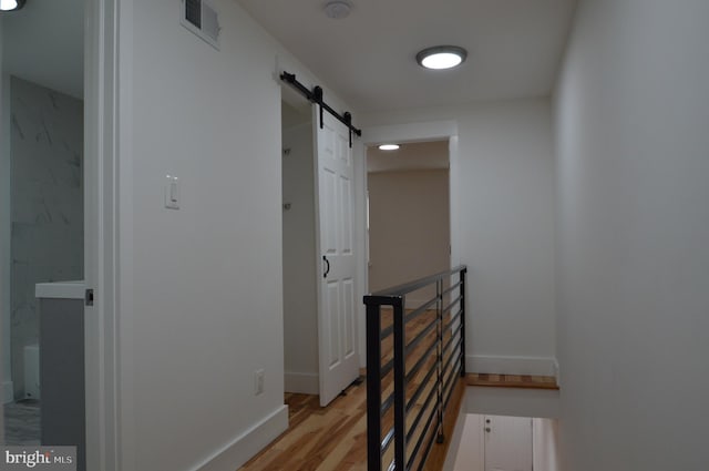 hall featuring a barn door, an upstairs landing, light wood finished floors, baseboards, and visible vents