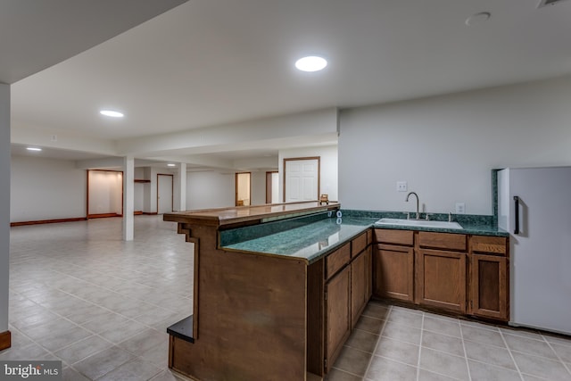 kitchen with kitchen peninsula, white fridge, sink, and light tile patterned floors