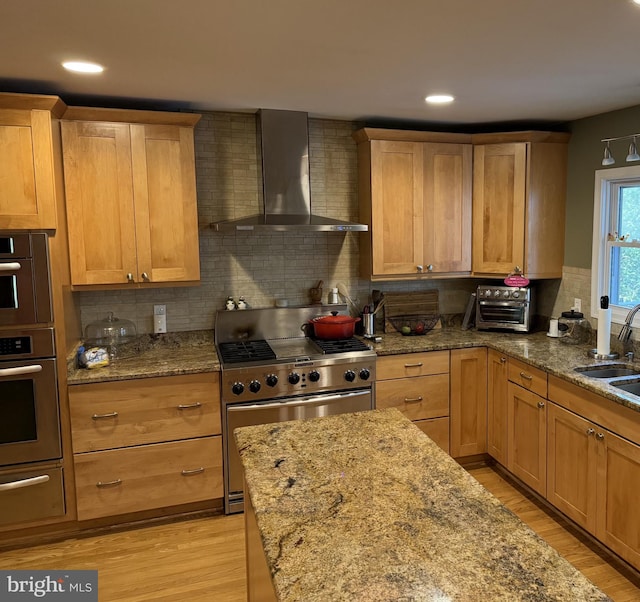 kitchen with wall chimney exhaust hood, light hardwood / wood-style floors, light stone countertops, and stainless steel stove