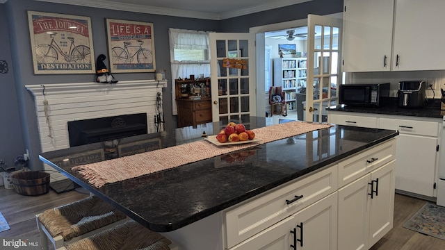 kitchen featuring white cabinetry, dark wood-type flooring, dark stone countertops, a kitchen bar, and ornamental molding