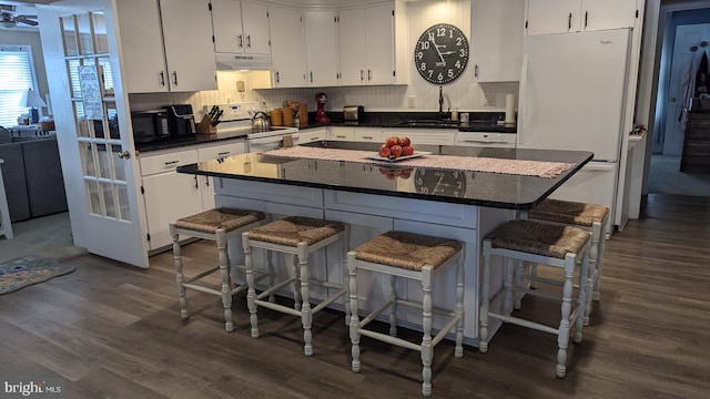 kitchen featuring white cabinets, a kitchen bar, white appliances, and dark wood-type flooring