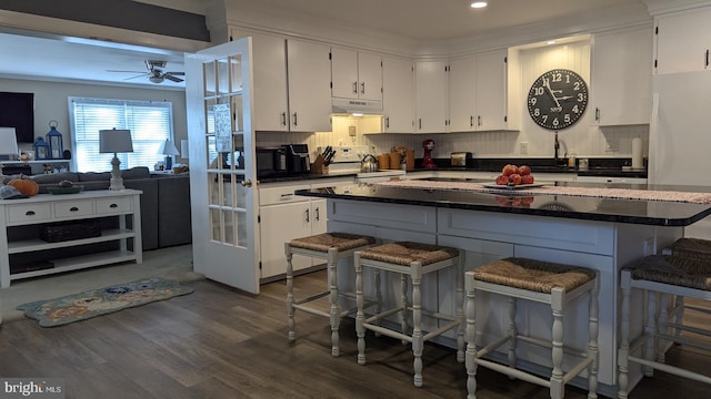 kitchen with a kitchen bar, stove, dark hardwood / wood-style flooring, white refrigerator, and white cabinets